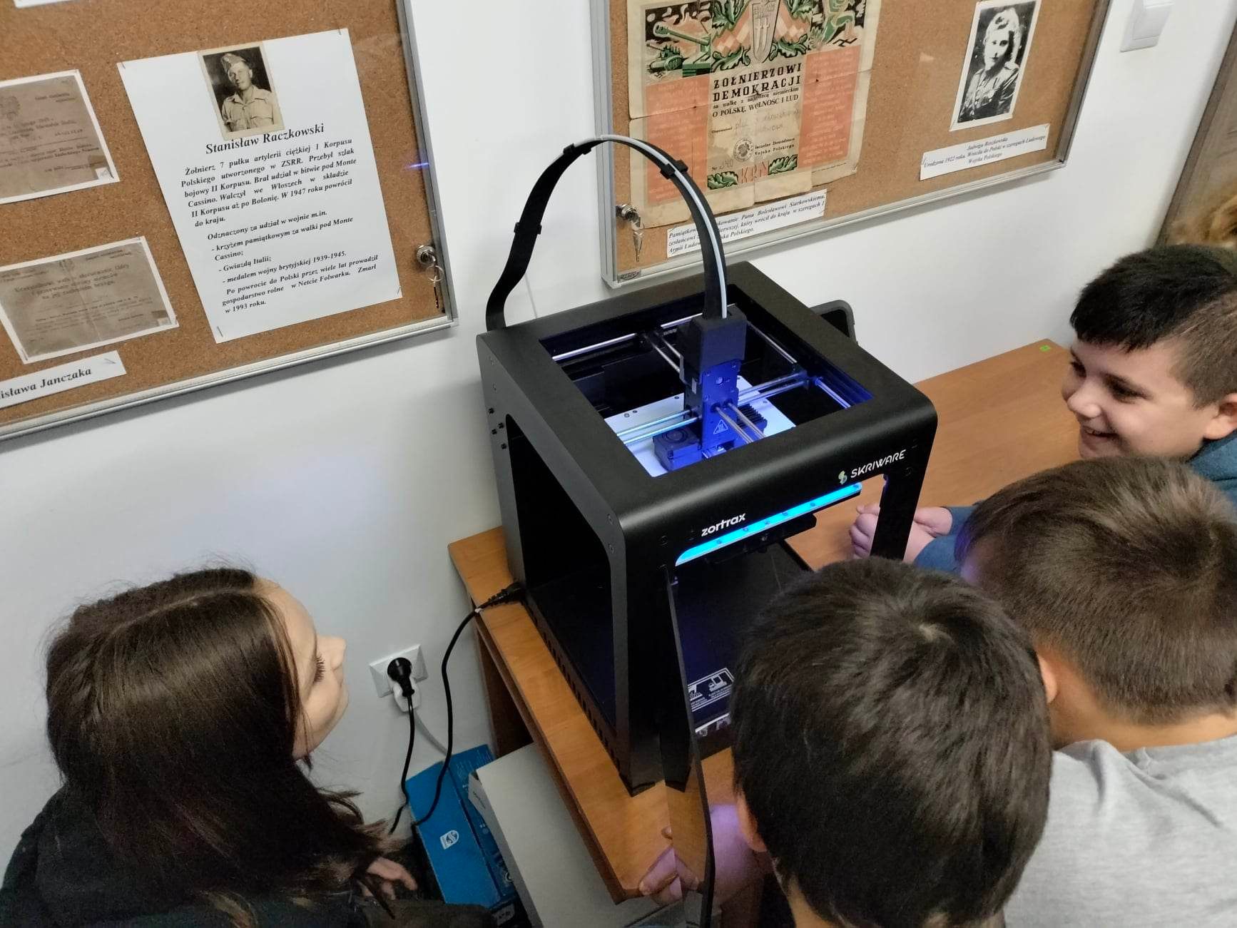 Czworo uczniów przygląda się pracy drukarki 3D.
