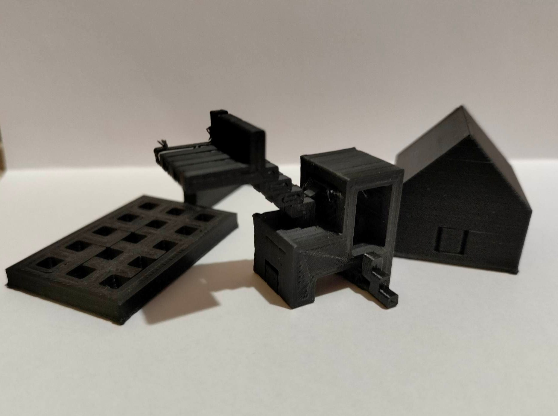 3 czarne figurki wydrukowane na drukarce 3D - łapka, koparka i domek.