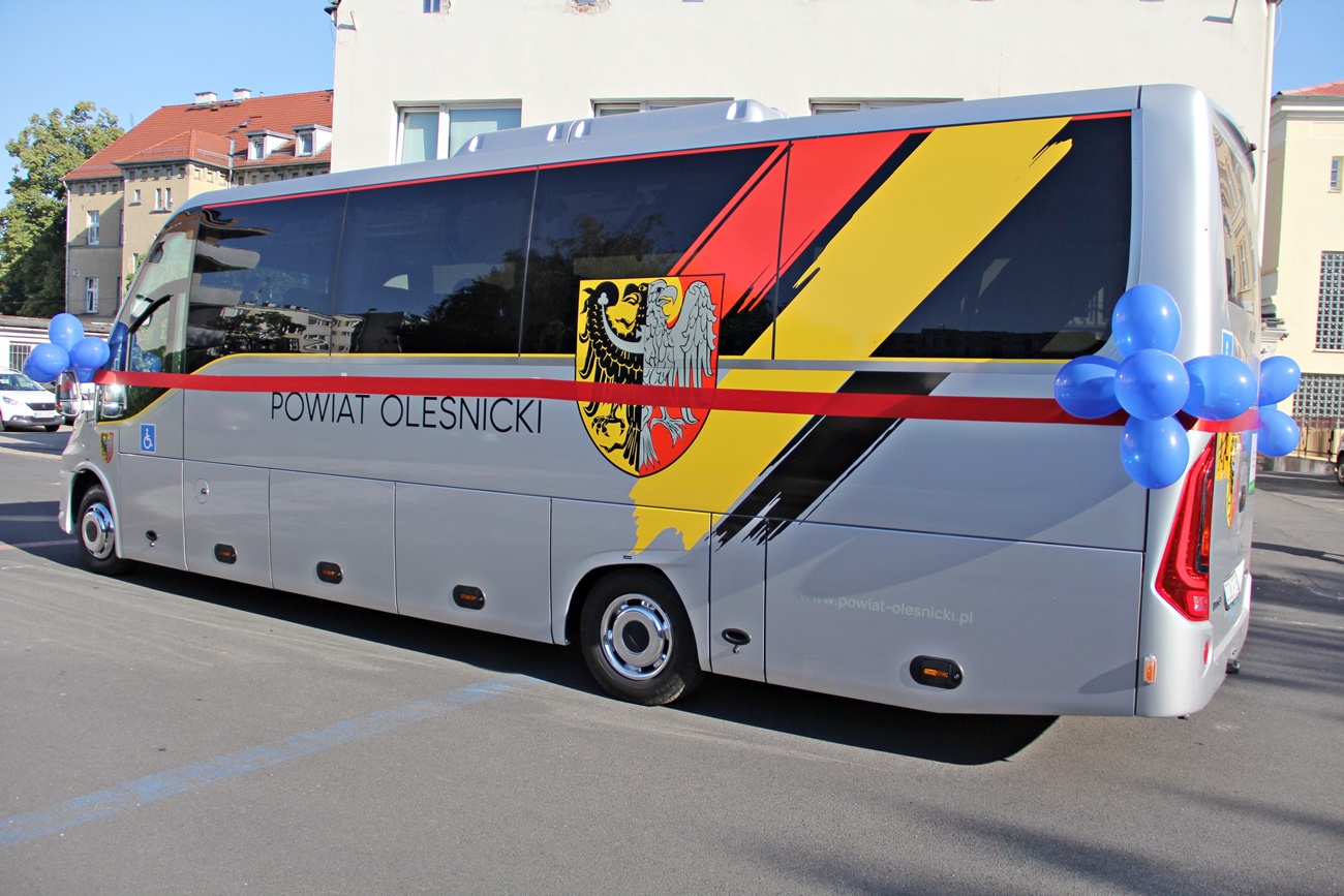 Autobus oklejony w barwy herbu powiatu stoi na placu przed szkoła