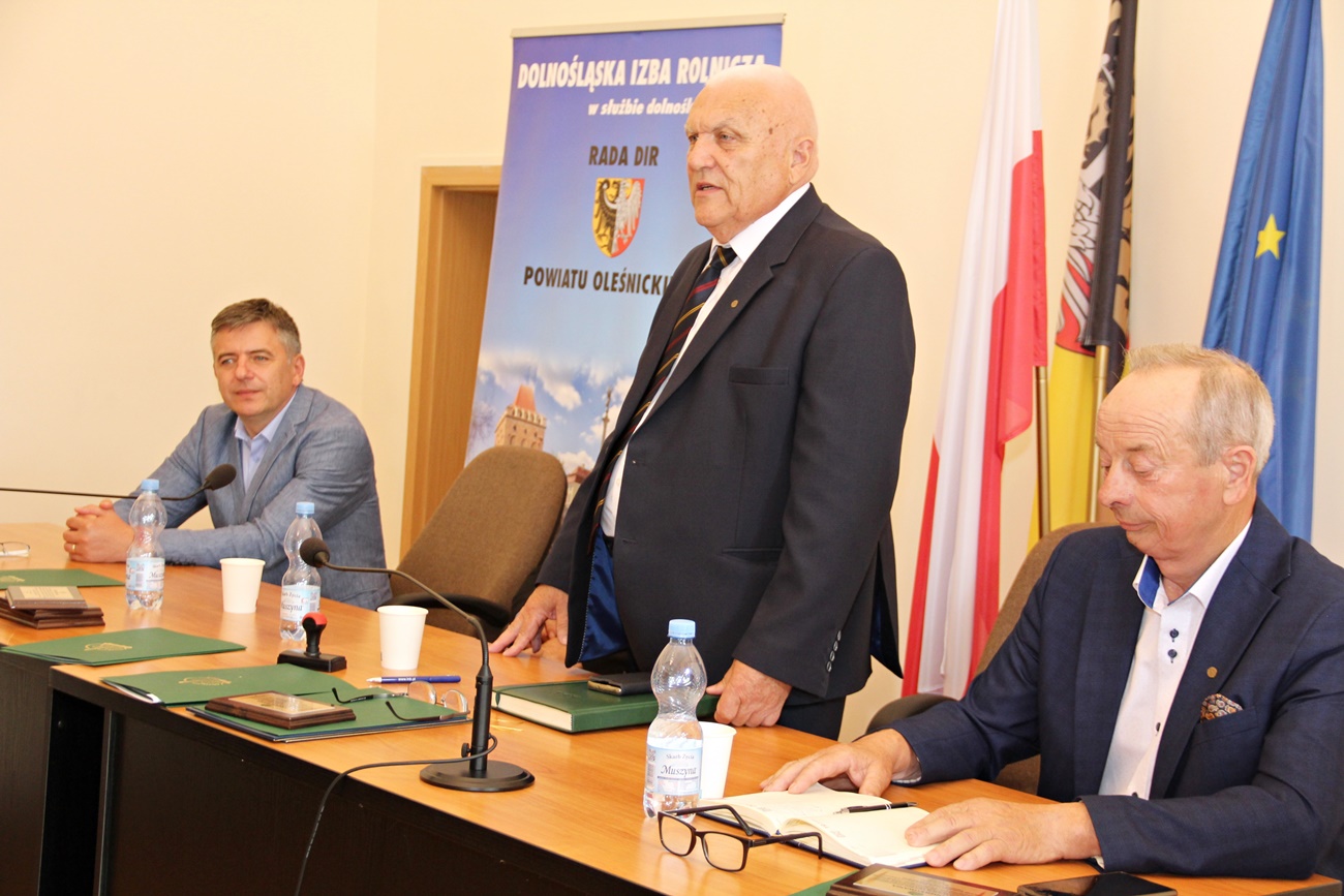 Przy prezydialnym stole, stojąc, gości wita przewodniczący