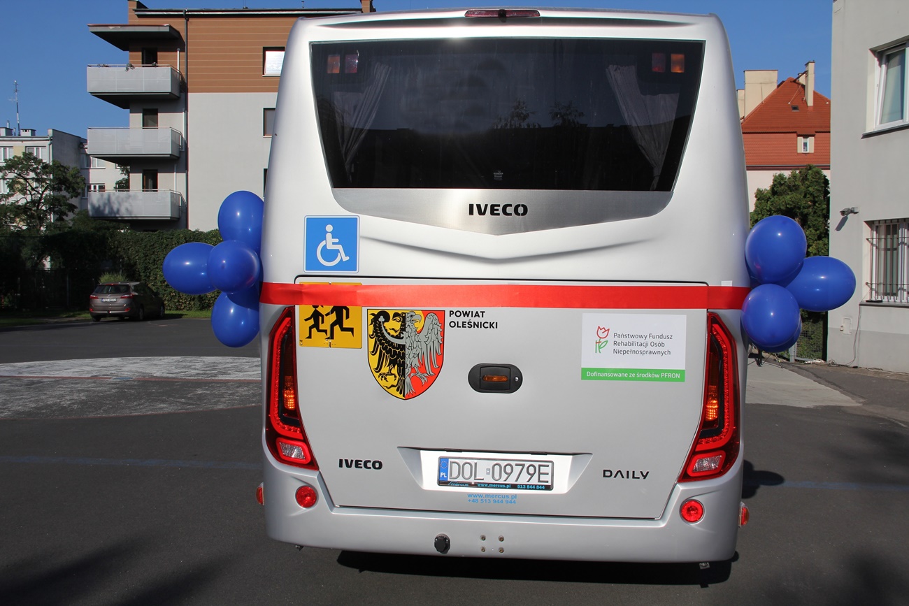 Autobus oklejony w barwy herbu powiatu stoi na placu przed szkołą