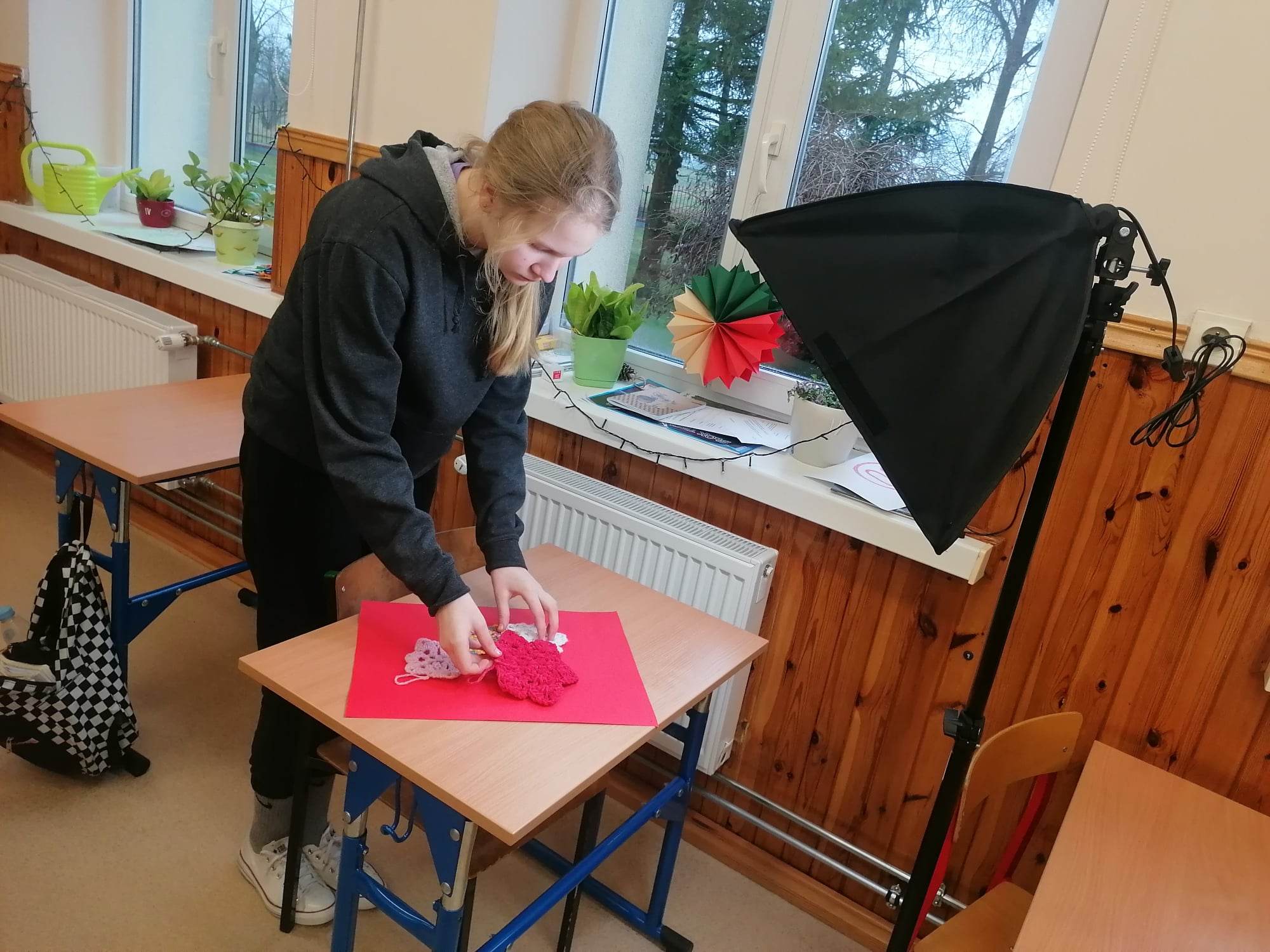 Dziewczyna układa na czerwonej serwetce wykonane na szydełku bombki. Obok stoi lampa fotograficzna.