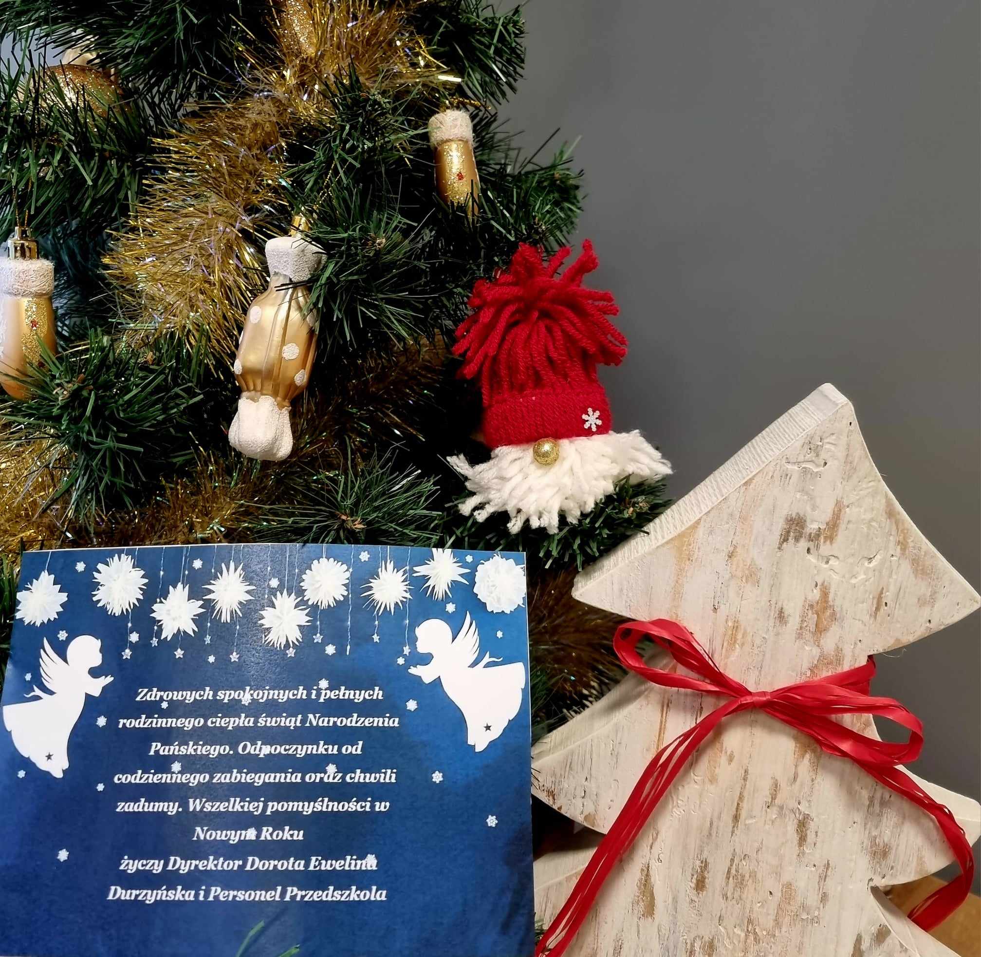 Świąteczne życzenia od społeczności Przedszkola stoją na tle choinek