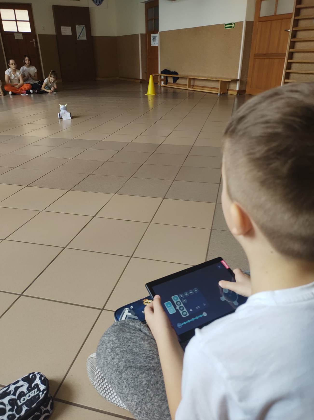 Uczeń siedzi na podłodze i za pomocą tabletu steruje robotem Photon.