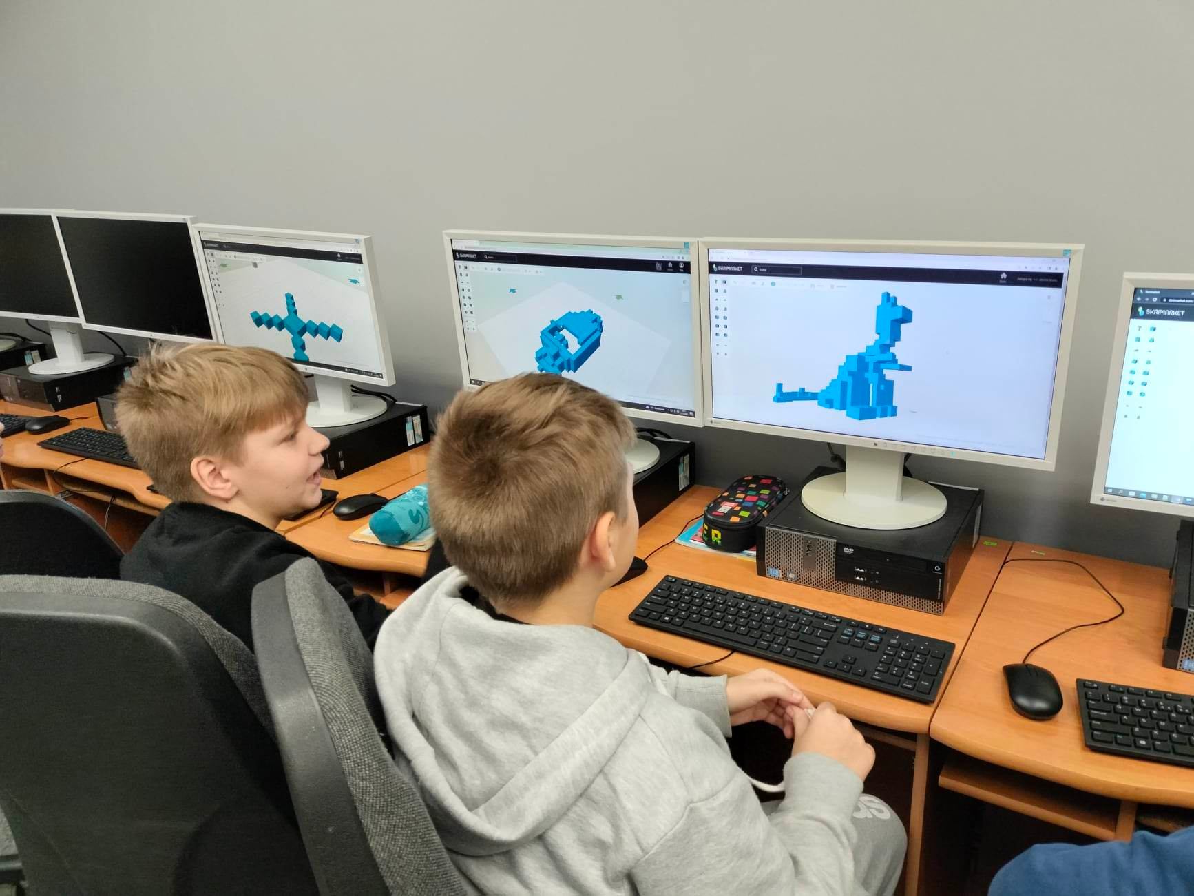Dwóch chłopców projektuje na komputerach figurki do wydrukowania na drukarce 3D.
