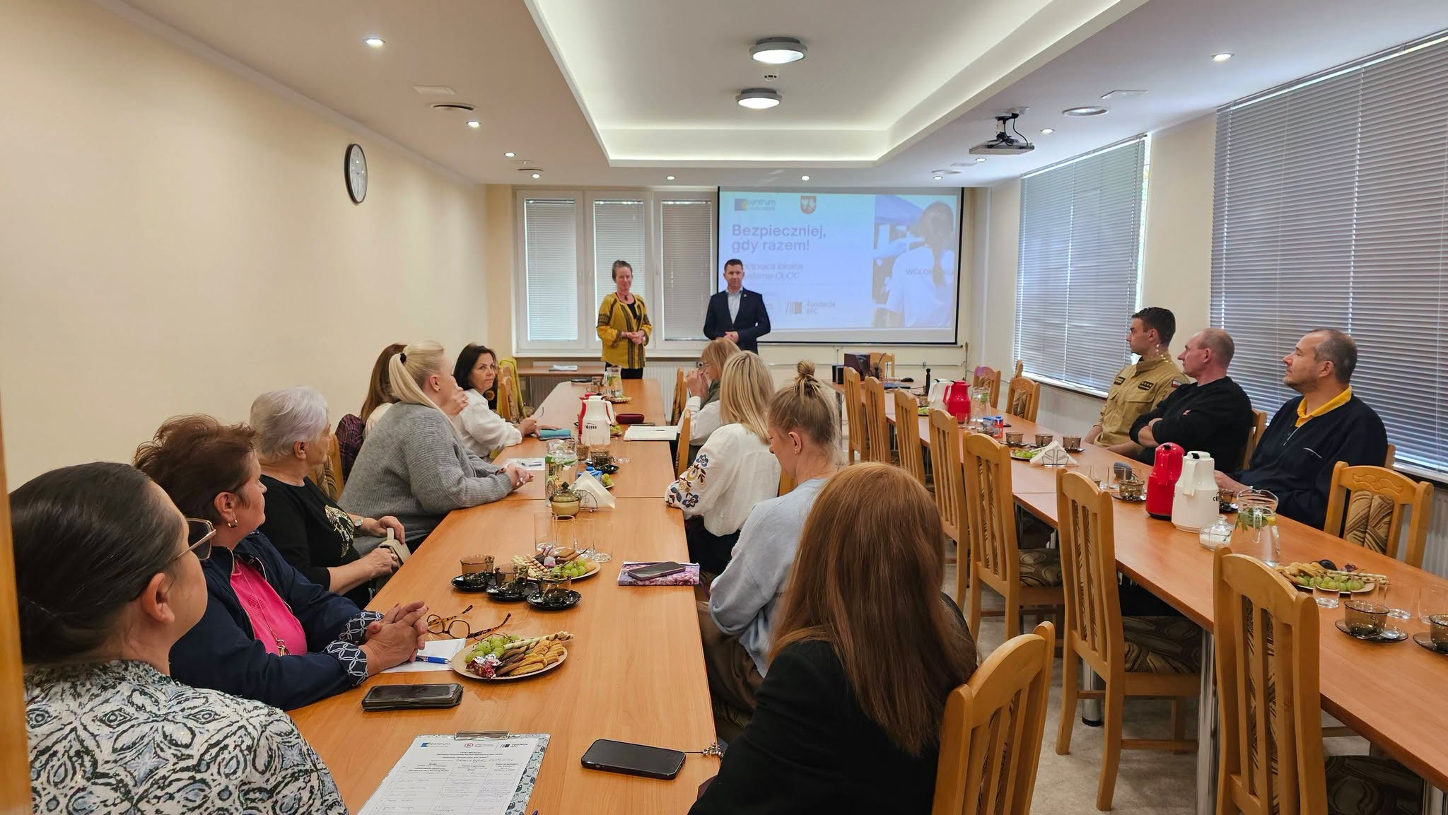 Grupa osób siedzących przy długim stole w sali konferencyjnej, a na ekranie z przodu wyświetlana jest prezentacja.