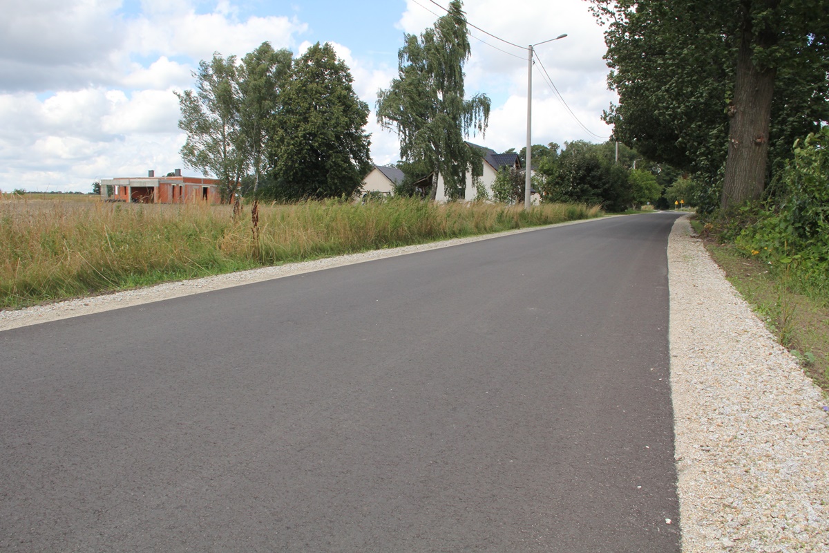 Nowy asfalt na drodze ciągnie się kilometrami. Po obu stronach białe pobocza, w tle drzewa, łąki i domy