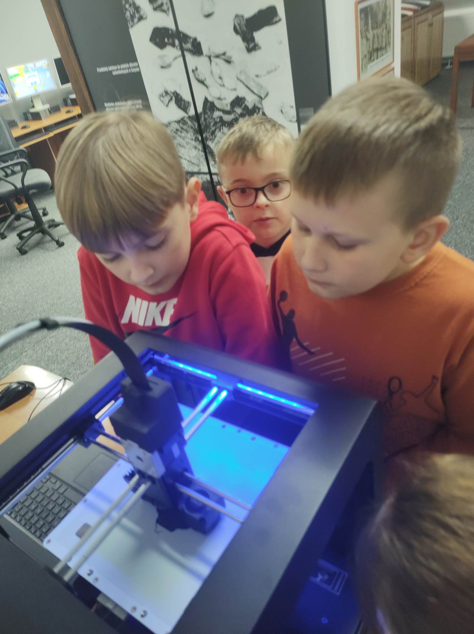 Troje uczniów przygląda się pracy drukarki 3d.
