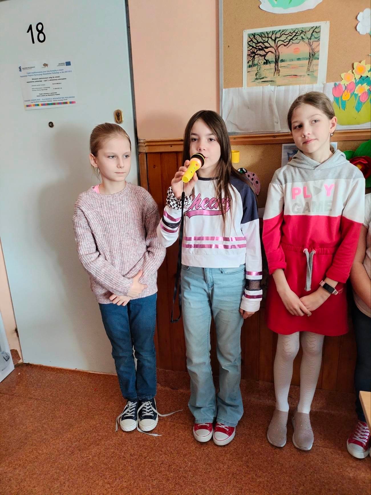 Dziewczynka trzyma w dłoni żółty mikrofon do którego mówi.