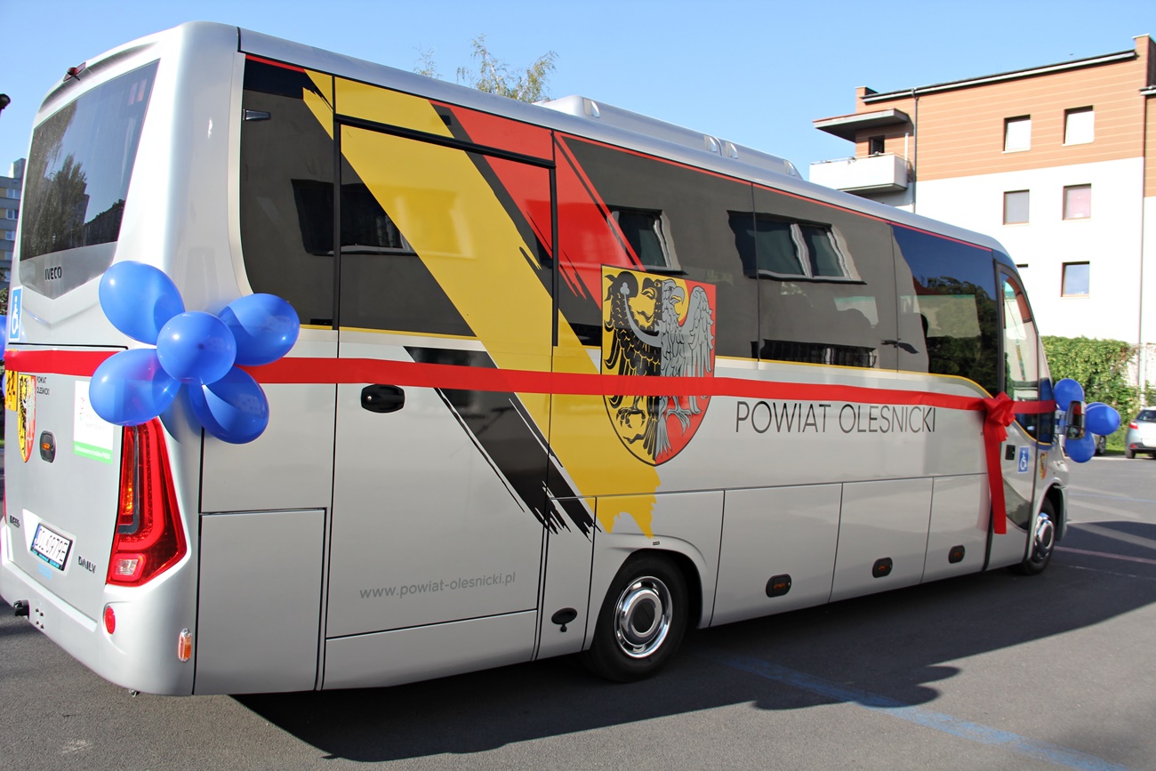 Autobus oklejony w barwy herbu powiatu stoi na placu przed szkoła