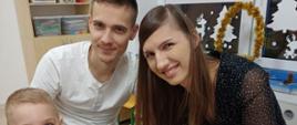 Rodzice z dzieckiem pozują do wspólnego zdjęcia w trakcie warsztatów plastycznych