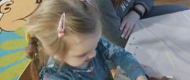 Uczestnicy warsztatów siedzą przy stole, dekorują pierniczki