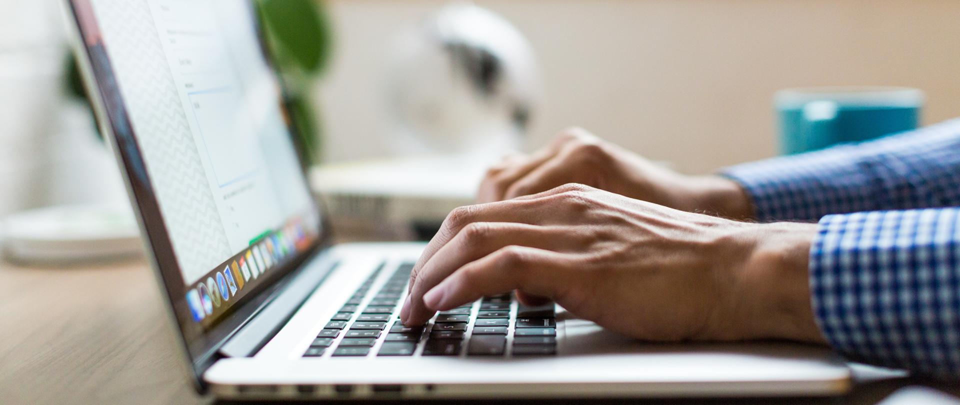 dłonie mężczyzny piszącego na klawiaturze laptopa