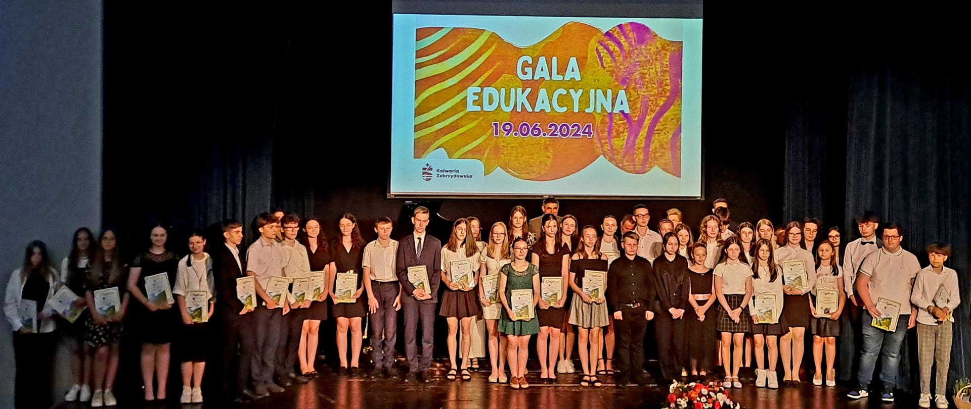 Na scenie stoją nagrodzeni uczniowie ze szkół z terenu Gminy Kalwaria Zebrzydowska wytypowani przez Dyrektorów poszczególnych szkół za największe osiągnięcia