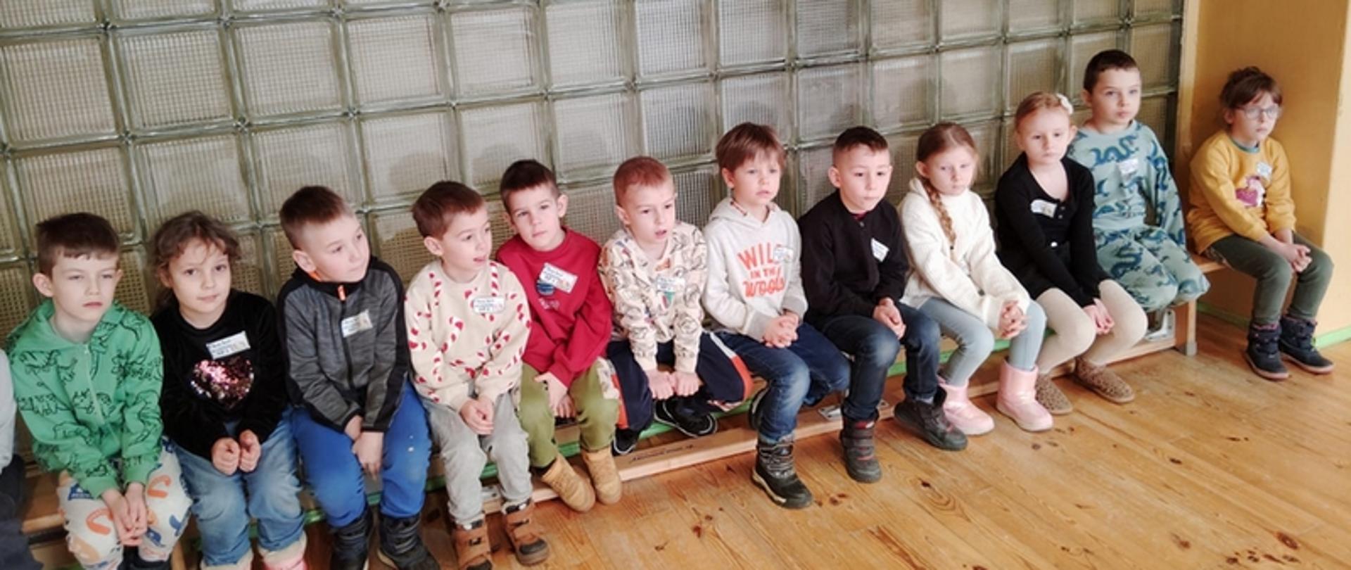 Dzieci siedzą na ławce w sali gimnastycznej 