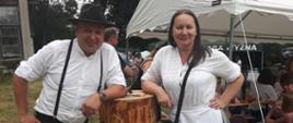 Dwie osoby stoją obok pnia i opierają się na nim jedną ręką, pozując do zdjęcia. Po lewej od pnia stoi Krystian Luberda, a po prawej Małgorzata Szarlej. Na pniu jest wyrzeźbiona pszczoła i kwiatek