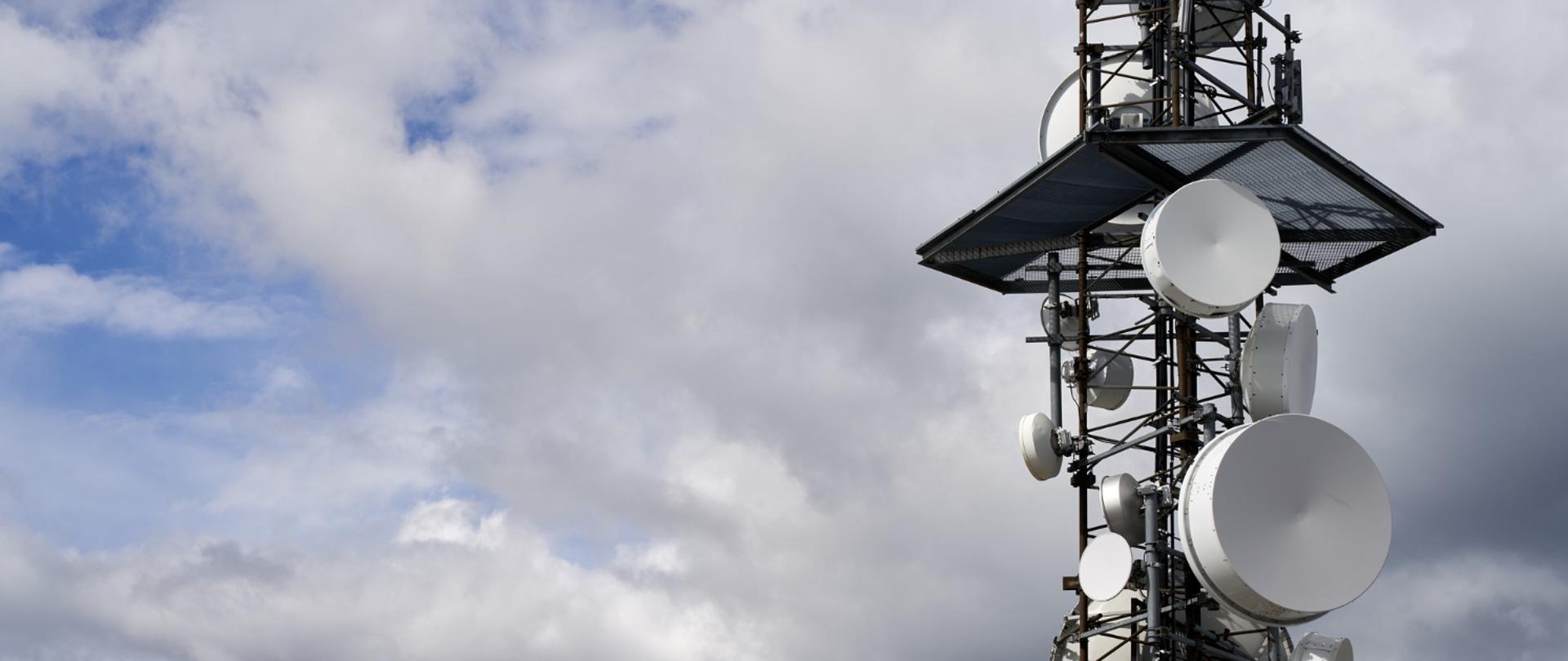 Wieża telekomunikacyjna na tle nieba i chmur.