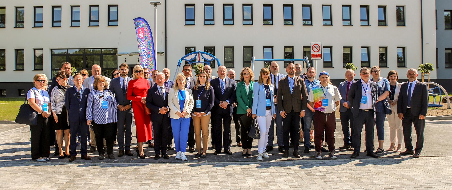 Zdjęcie przedstawia grupę ludzi pozujących do pamiątkowego zdjęcie przed budynkiem.