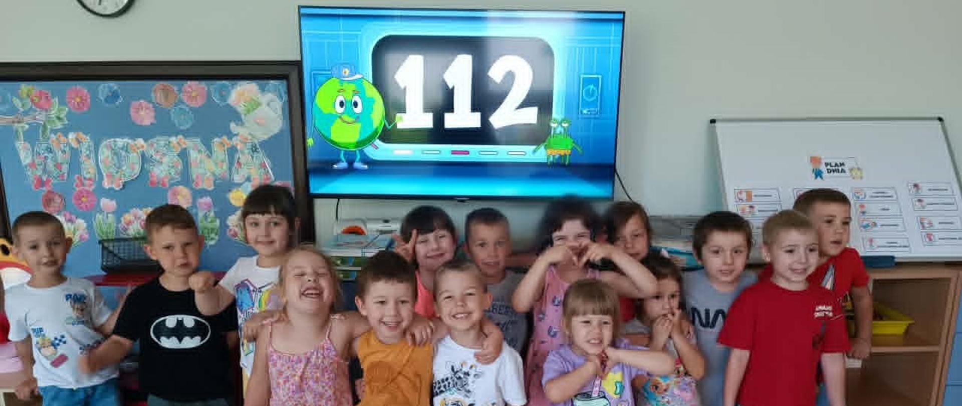 Dzieci pozują do zdjęcia, w tle numer 112 na pulpicie