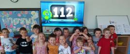 Dzieci pozują do zdjęcia, w tle numer 112 na pulpicie