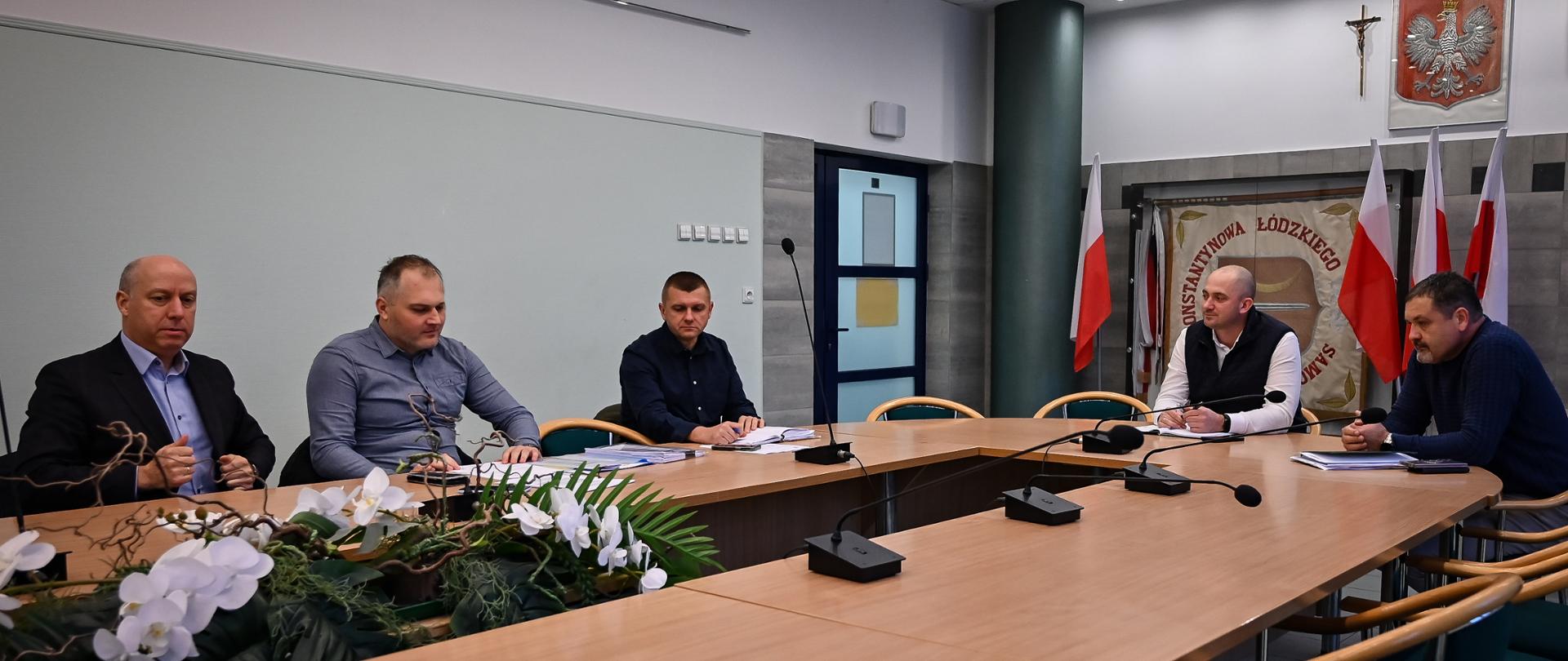 Pięciu mężczyzn siedzi przy stole w sali konferencyjnej.