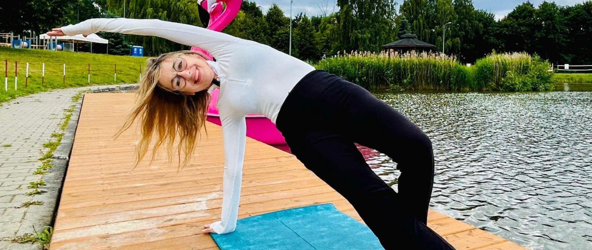 Kobieta trenująca jogę na pomoście nad stawem.