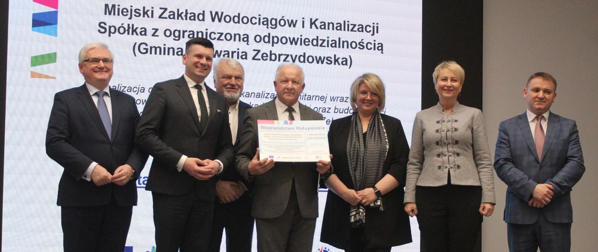 Zdjęcie grupowe z wręczenia dotacji w wysokości 1 mln 544 tys. zł na budowę kanalizacji sanitarnej i wodociągowej. Stoją wicemarszałkowie Łukasz Smółka i Józef Gawron, Iwona Gibas z zarządu województwa i radny województwa Stanisław Bisztyga 