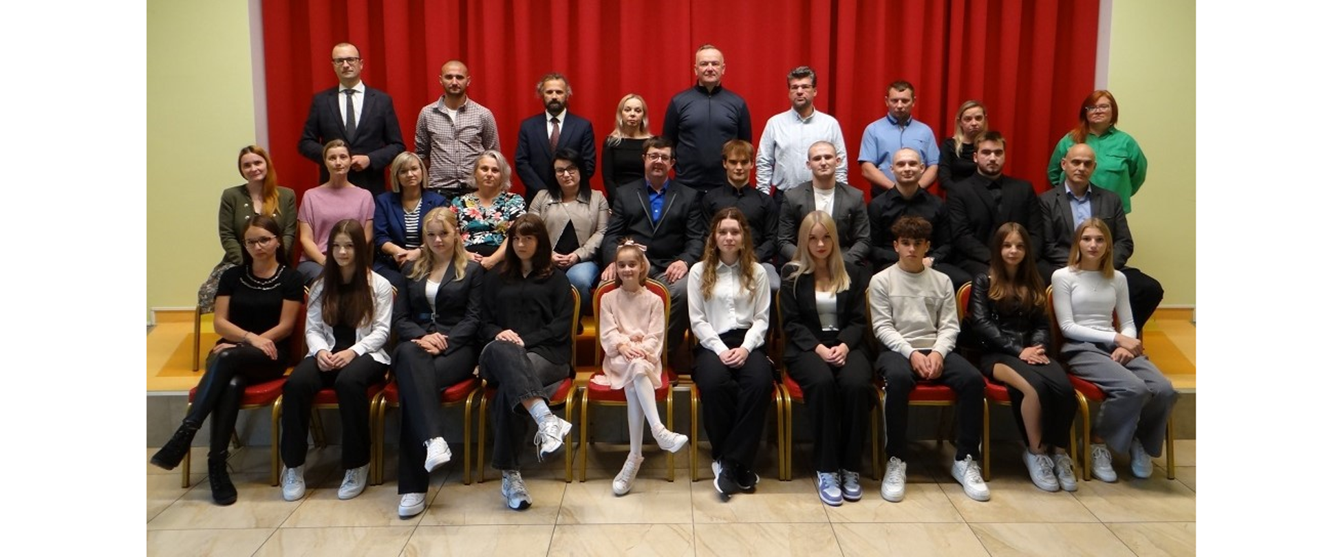 Wspólna fotografia sportowców z ich rodzicami i przedstawicielami władz Gminy Hażlach. Osoby pozujące do fotografii siedzą w dwóch rzędach na krzesłach oraz stoją na scenie