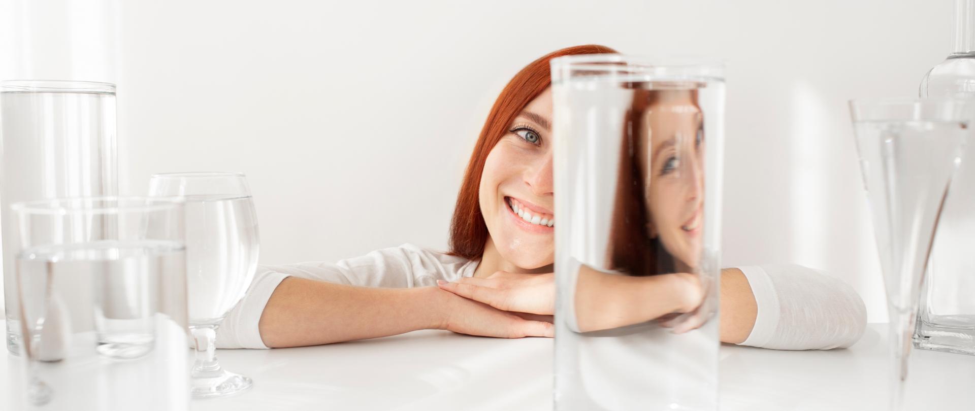 Kobieta patrzy przez szklankę z czystą wodą.