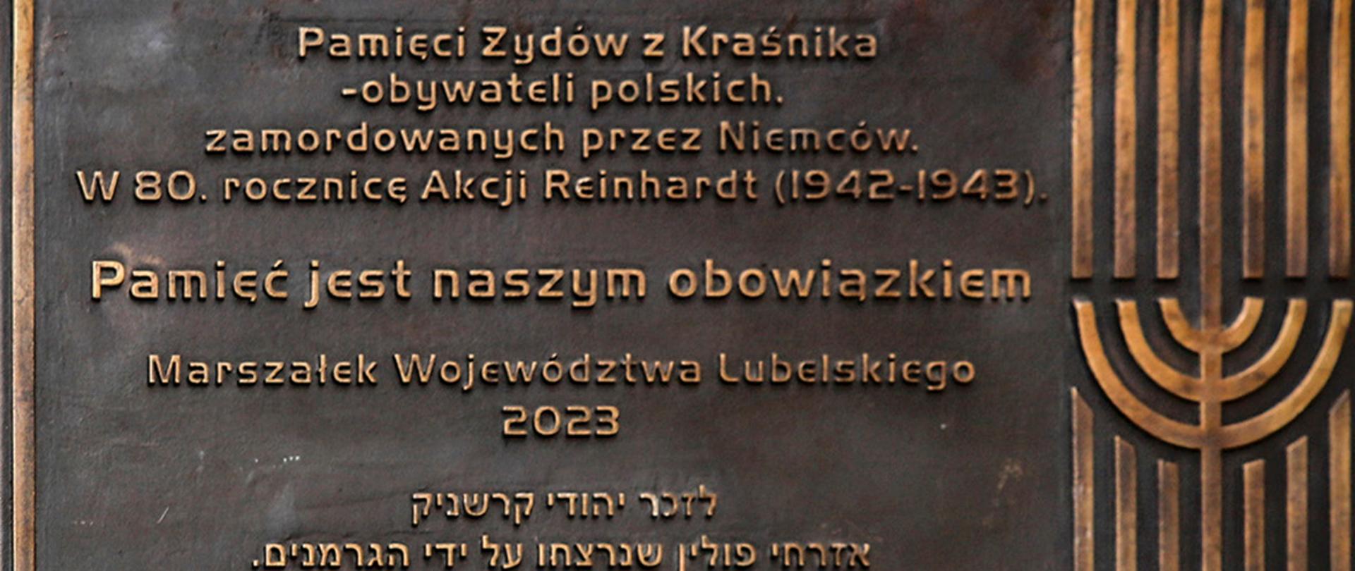 Zdjęcie przedstawia mosiężną tablicę, na której znajdują się napisy w języku polskim oraz jidysz. Polski napis głosi: "Pamięci Żydów z Kraśnika - obywateli polskich, zamordowanych przez Niemców. W 80. rocznicę Akcji Reinhardt (1942-1943). Pamięć jest naszym obowiązkiem - Marszałek Województwa Lubelskiego 2023".
