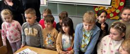 Dzieci stoją przy stole, na których leżą materiały edukacyjne
