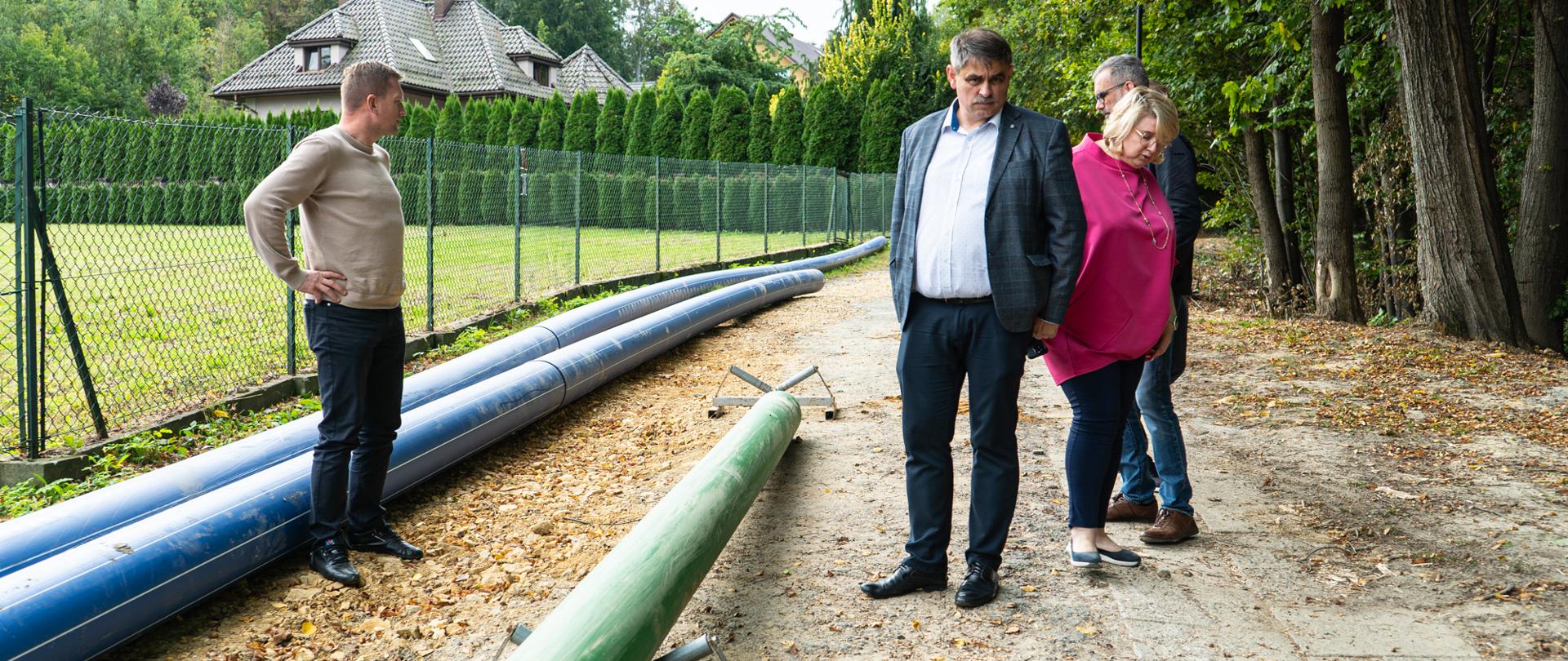 Na zdjęciu znajdują się cztery osoby, w tym Burmistrz Miasta Kalwarii Zebrzydowskiej, które obserwują postęp prac związanych z rozbudową kanalizacji w rejonie ul. Błażkówka oraz ul. Kościuszki.