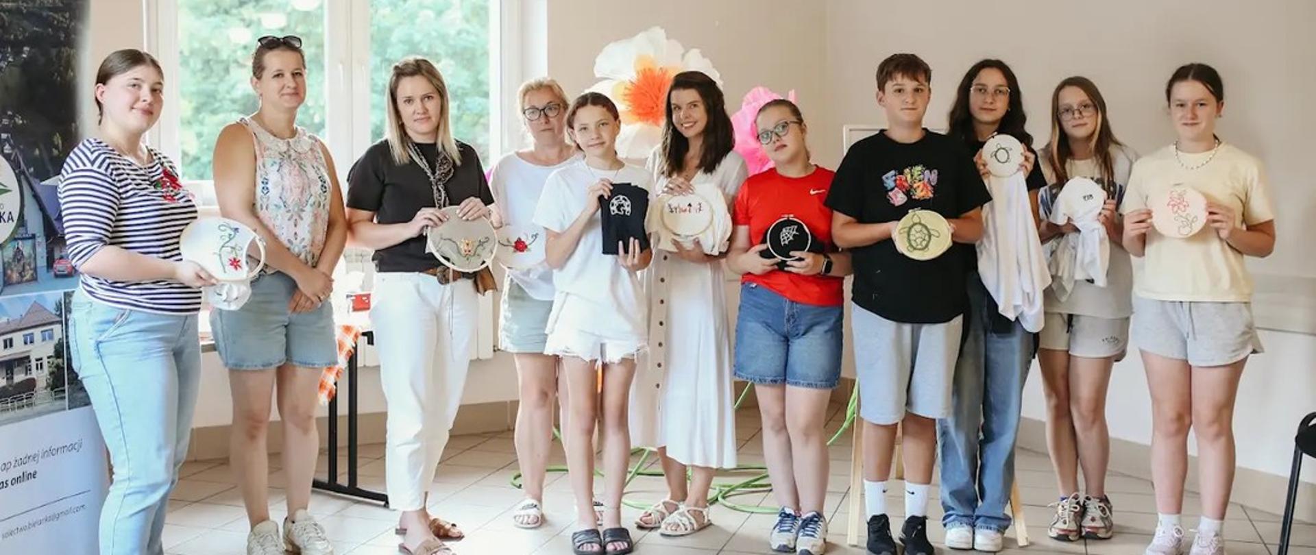 Grupa osób prezentująca swoje prace z haftu.