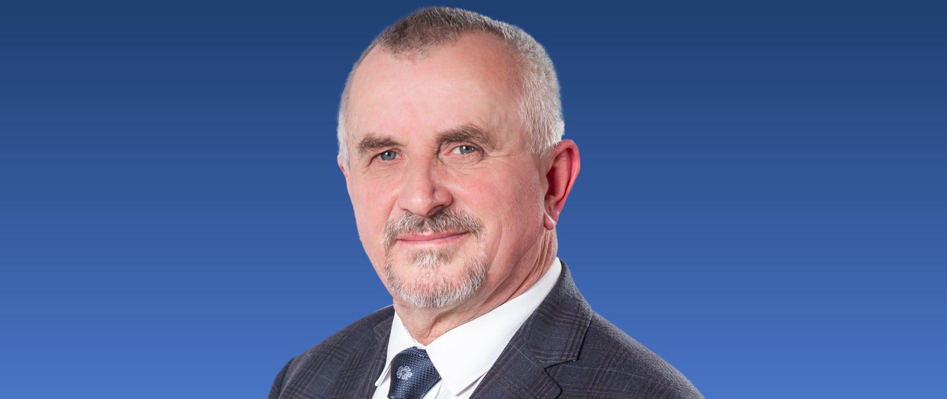 Zdjęcie przedstawia mężczyznę w krawacie na niebieskim tle.