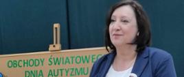 Zdjęcie przedstawia Panią Dyrektor Annę Niekrę stojącą na auli szkoły. W tle ustawiona jest tablica informująca o obchodach Światowego Dnia Autyzmu i Dnia Otwartego w Zespole Szkół Specjalnych w Kraśniku. 