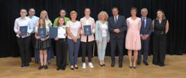 Uczniowie ze szkoły w Bielance wspólnie z p. dyrektor, panem wójtem, zastępcą wójta, panią Ewą Miśkowiec oraz pracownikiem ZEAS. Wszyscy pozują do zdjęcia na scenie w remizie OSP.