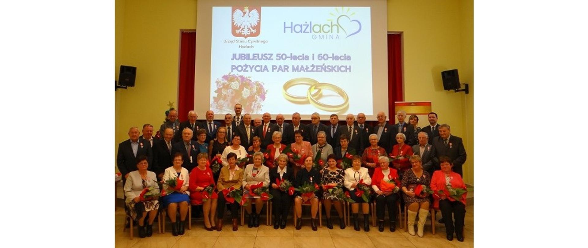 Pamiątkowa fotografia uczestników spotkania. Zebrani siedzą na krzesłach w jednym rzędzie oraz stoją z tyłu.