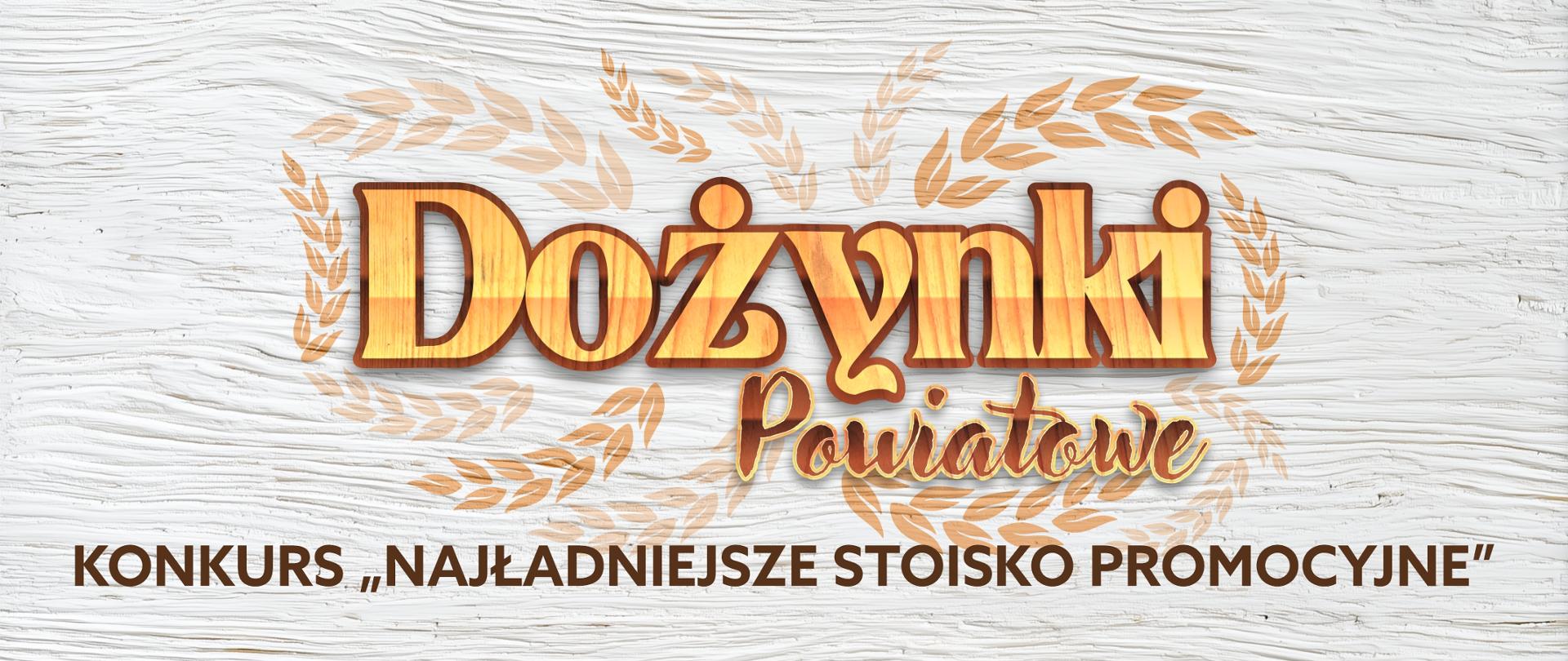 Grafika przedstawia pomalowaną białą deskę, na której znajduje się otoczony wizerunkami kłosów zbóż napis "Dożynki Powiatowe", a pod nim nazwa konkursu "Konkurs na najładniejsze stoisko promocyjne" w kolorze brązowym.