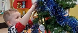 Chłopczyk stoi przy choince, dekoruje ją