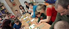 Rodzice z dziećmi siedzą przy stole, przygotowują gwiazdy z papieru