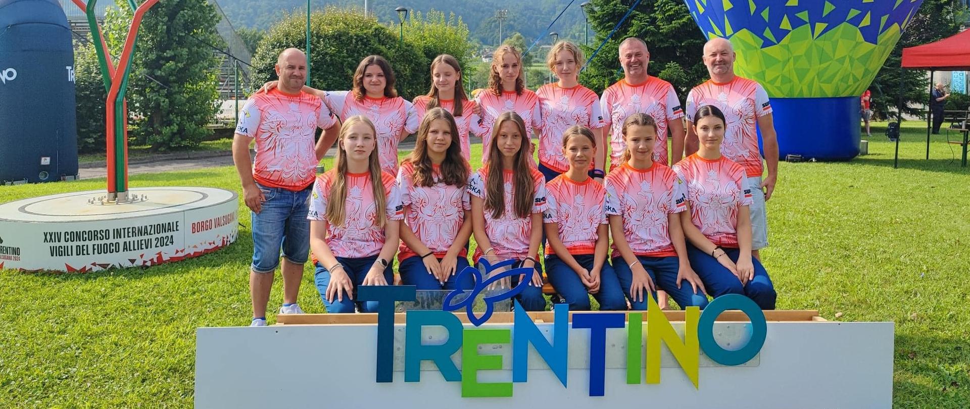 Grupa dziewcząt i opiekunów na tle gór z przodu napis Trentino