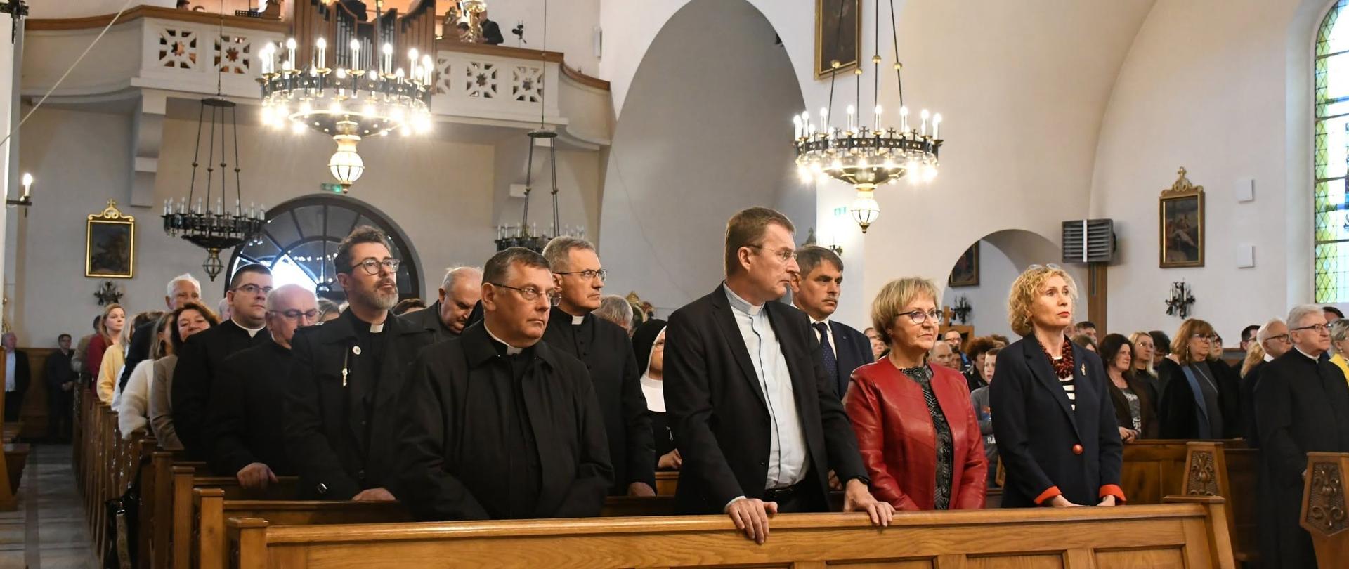 Festiwal organowy w kościele w Niegowici na zdjęciu zaproszenie goście kobiety i mężczyźnie w drugiej ławce m.in, burmistrz Kalwarii Zebrzydowskiej Tadeusz Stele, w tle widać organy kościelne oraz piękne żyrandole. 
