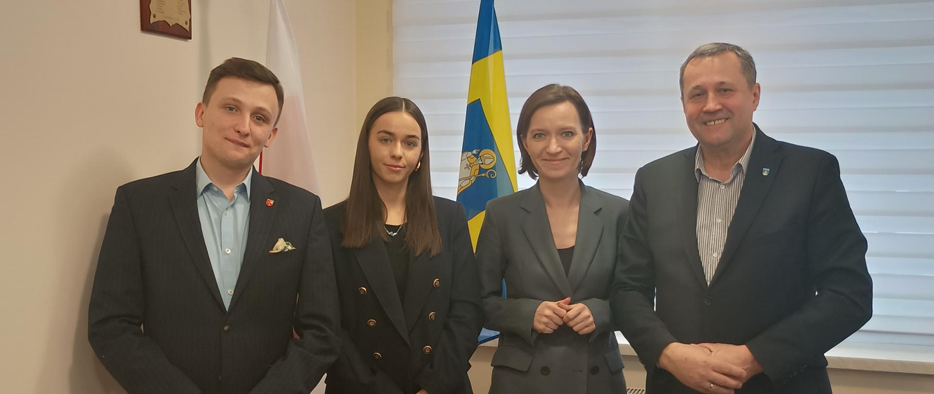 Dyżur poselski - Weronika Smarduch, Wójt, Radny Piotr Wójciak oraz pracownica biura poselskiego Aleksandra Mąka stoją pod flagą i herbem Gminy Raba Wyżna 