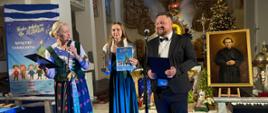 Moment wręczenie nagród,. dwoje prowadzących przemawia do mikrofonu. Po środku laureatka z dyplomem. 