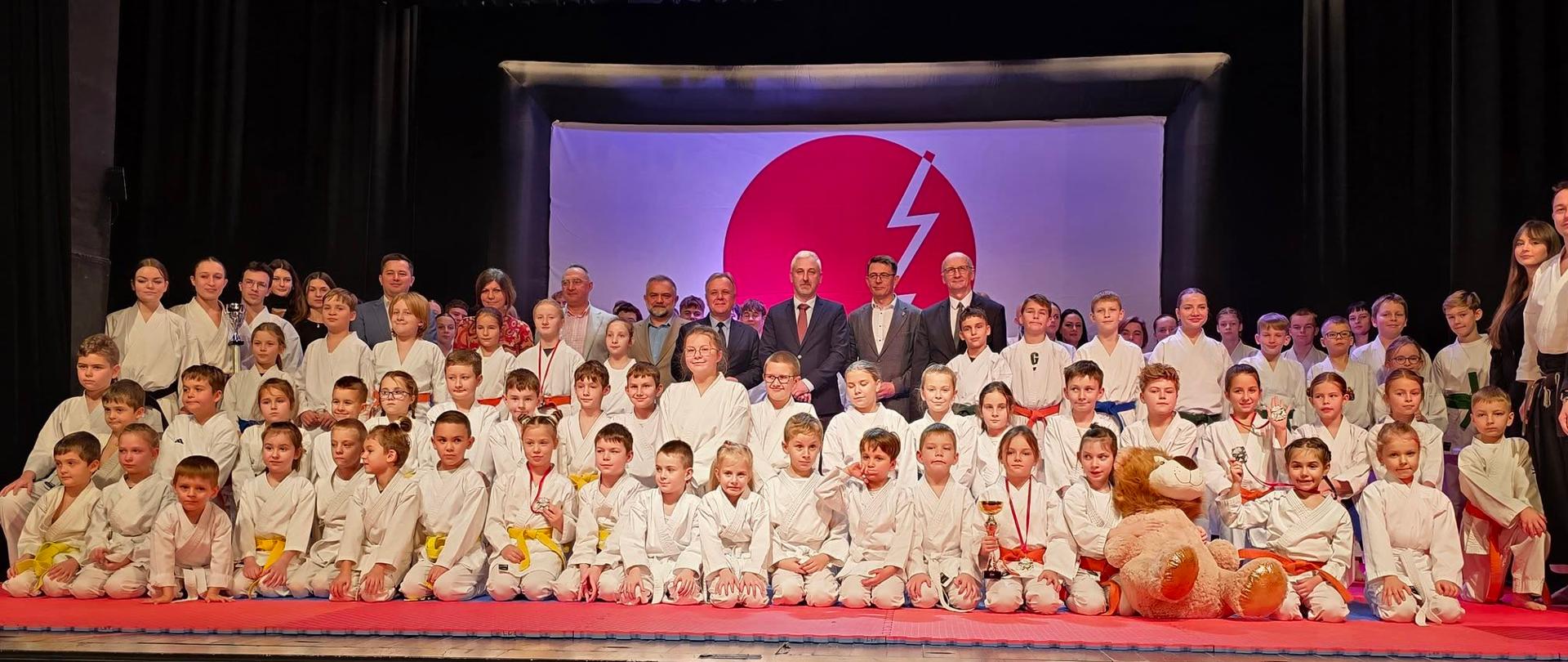 Zawodnicy Klubu Karate Tradycyjnego Chidori ustawieni na scenie Centrum Kultury i Promocji w Kraśniku. Po stronie prawej stoi trener i jednocześnie prezes klubu Marek Bury. Pośrodku karateków stoją zaproszeni gości.