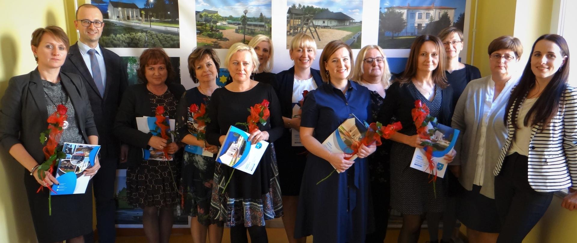 Uczestnicy spotkania w Urzędzie Gminy Hażlach. Zbiorowa fotografia na korytarzu budynku. Z tyłu baner promocyjny z fotografiami z terenu gminy Hażlach