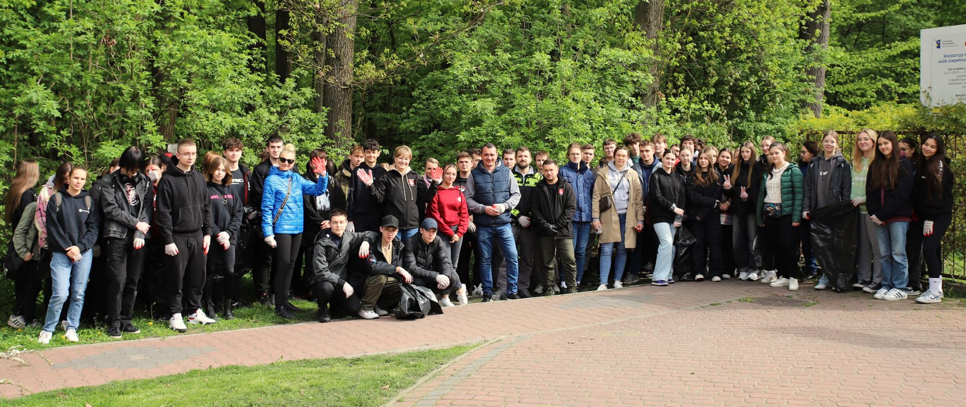 Na zdjęciu duża grupa uczniów i pracowników Starostwa Powiatowego pozuje do pamiątkowego zdjęcia na tle lasu.