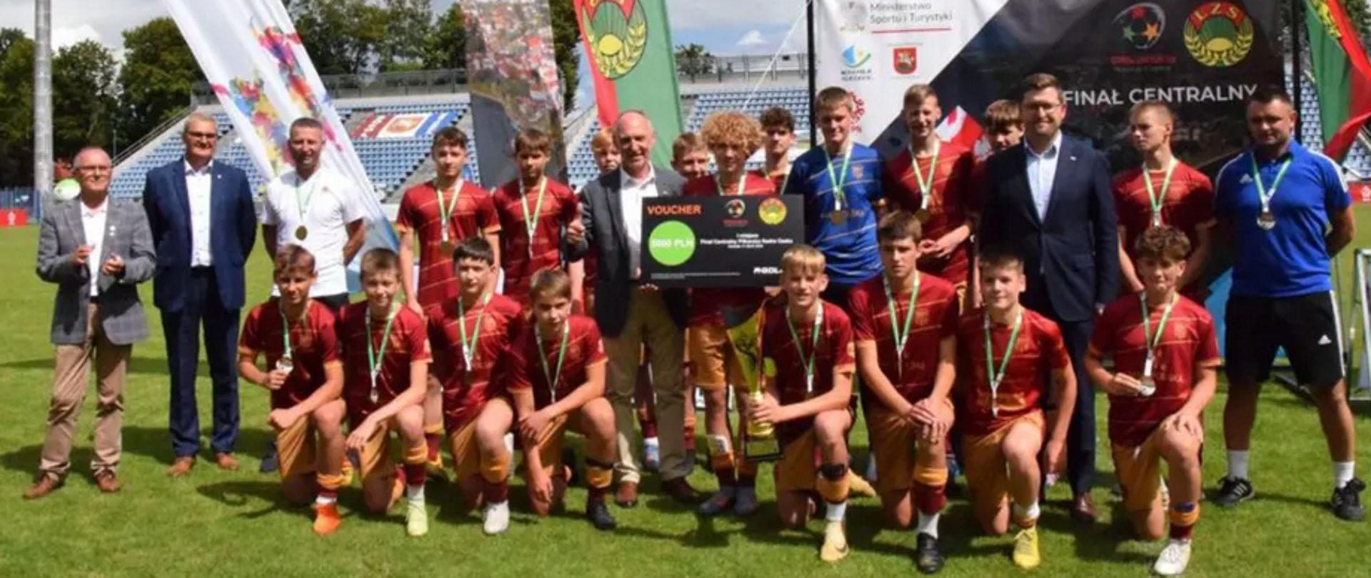 Grupa chłopów w strojach piłkarskich z medalami i pucharem 