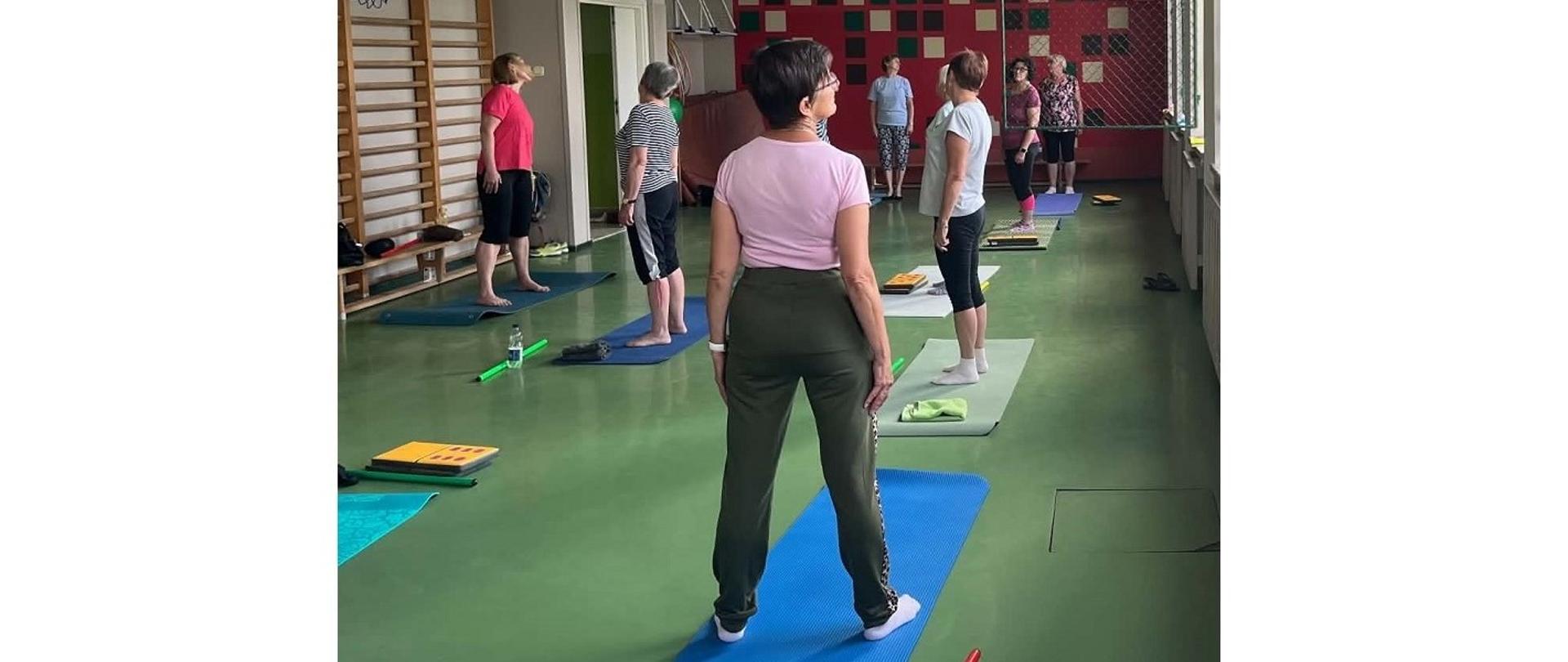 Zajęcia ruchowe – Zdrowy kręgosłup. Ubrane na sportowo dorosłe osoby ćwiczą w sali gimnastycznej 