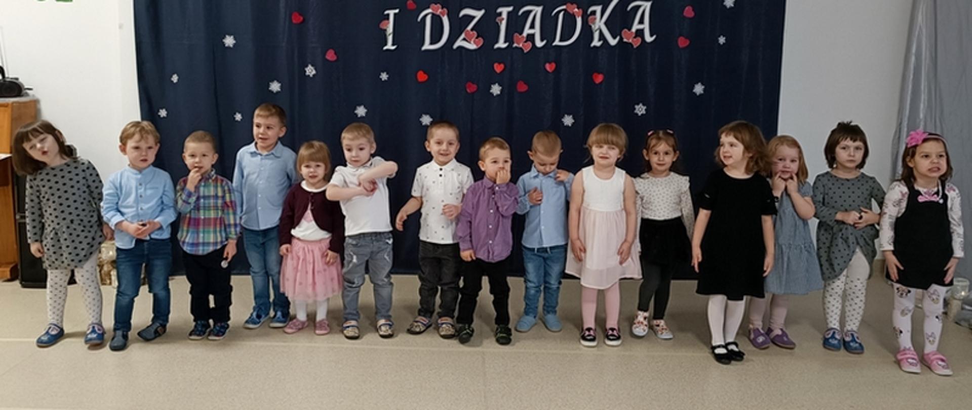 Dzieci w trakcie części artystycznej uroczystości - stoją w rzędzie, recytują i śpiewają.